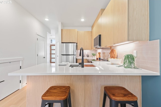 kitchen with stainless steel refrigerator, a kitchen bar, sink, and light brown cabinets