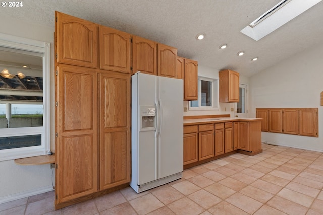 kitchen with a textured ceiling, light tile patterned floors, vaulted ceiling with skylight, and white refrigerator with ice dispenser