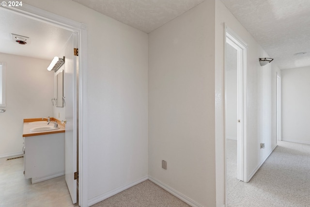 hallway featuring baseboards, visible vents, a textured ceiling, and a sink