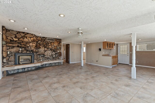 unfurnished living room with ceiling fan, light tile patterned flooring, sink, a textured ceiling, and a fireplace