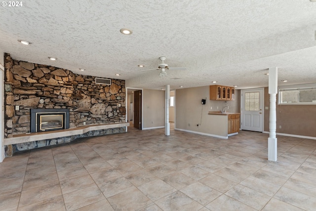 unfurnished living room with a textured ceiling, ceiling fan, visible vents, and a stone fireplace