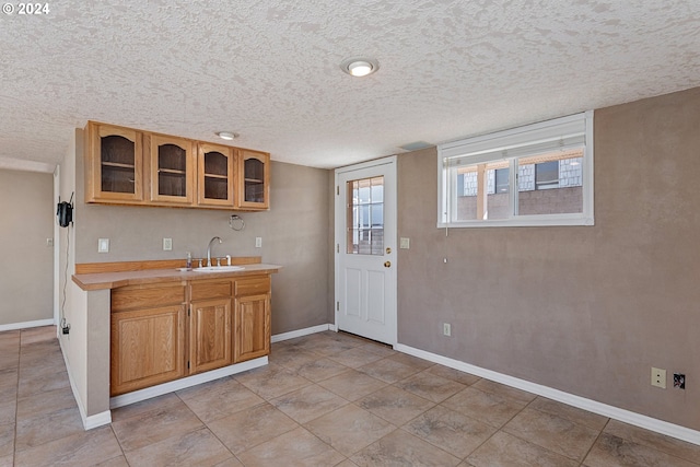kitchen with a textured ceiling, light countertops, glass insert cabinets, a sink, and brown cabinetry