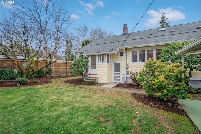 rear view of house with a yard, a chimney, a shingled roof, entry steps, and fence