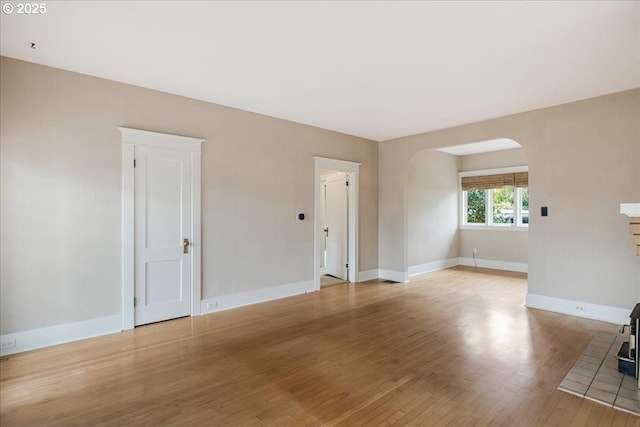 unfurnished living room with arched walkways, baseboards, and light wood finished floors