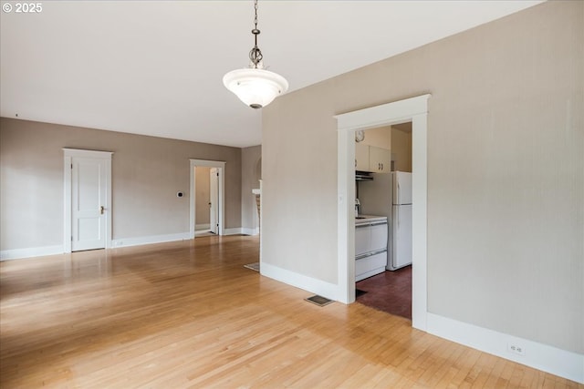 empty room with wood finished floors, visible vents, and baseboards