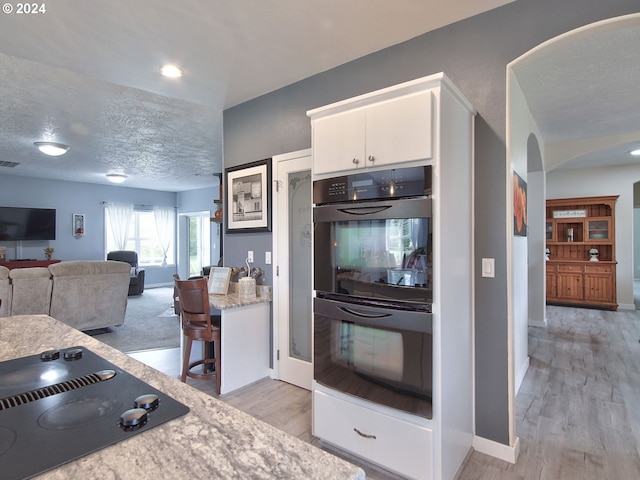 kitchen featuring light hardwood / wood-style flooring, white cabinets, black appliances, and a textured ceiling