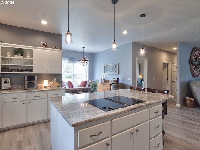 kitchen featuring light hardwood / wood-style flooring, black electric cooktop, decorative light fixtures, a kitchen island, and white cabinetry