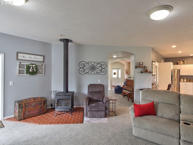 living room with a textured ceiling, a wood stove, and carpet floors