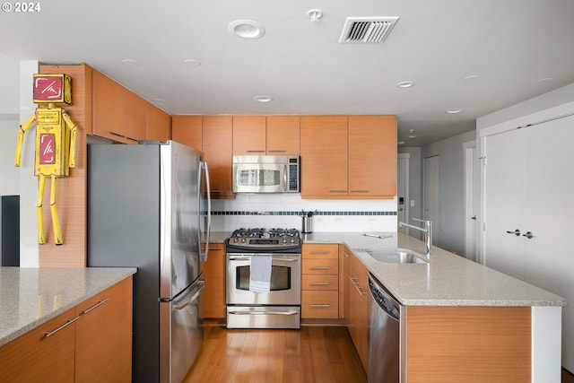 kitchen featuring backsplash, light stone countertops, sink, light hardwood / wood-style floors, and stainless steel appliances