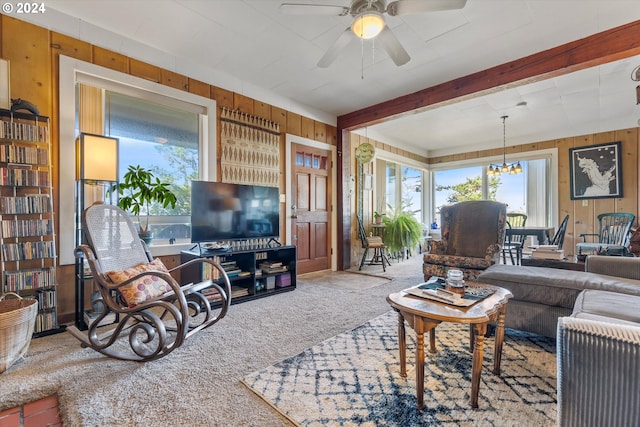 living room with carpet flooring, ceiling fan with notable chandelier, and wood walls