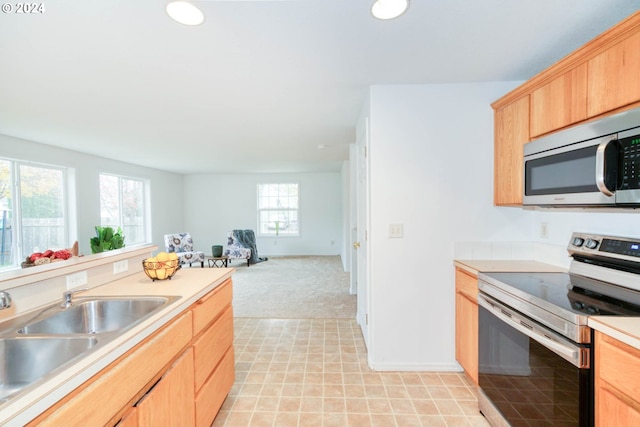 kitchen with stainless steel appliances, sink, light colored carpet, and light brown cabinetry