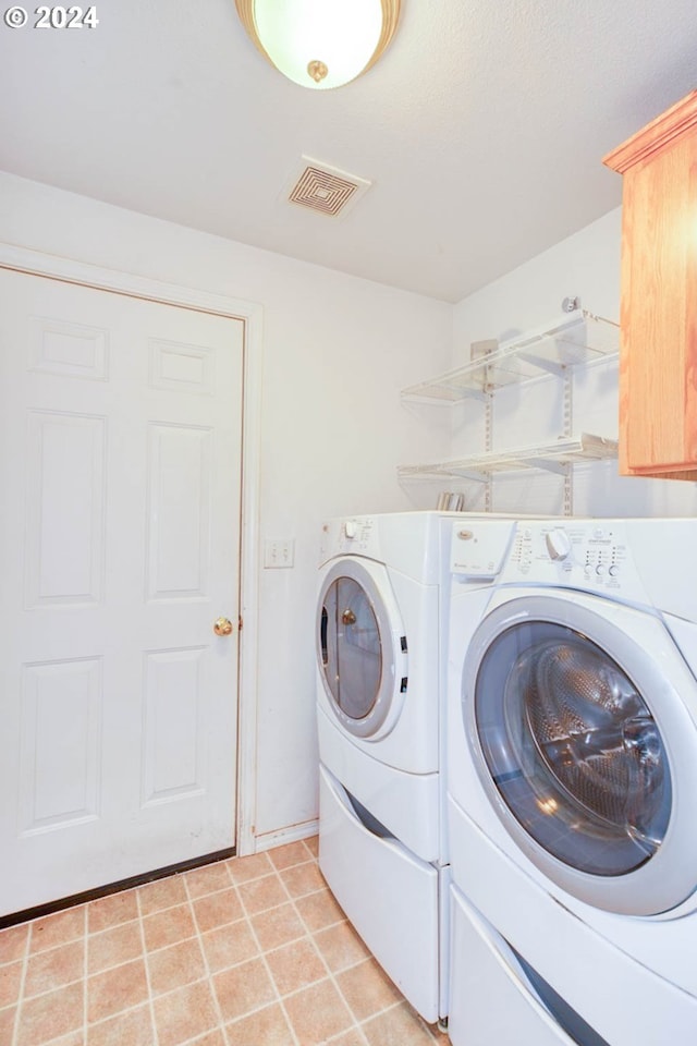 clothes washing area featuring separate washer and dryer, light tile patterned floors, and cabinets