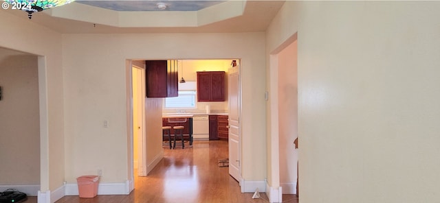 hall featuring a raised ceiling, sink, and light wood-type flooring