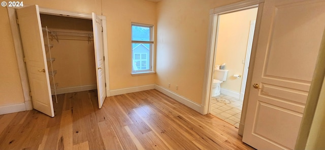 unfurnished bedroom with connected bathroom, a closet, and light wood-type flooring