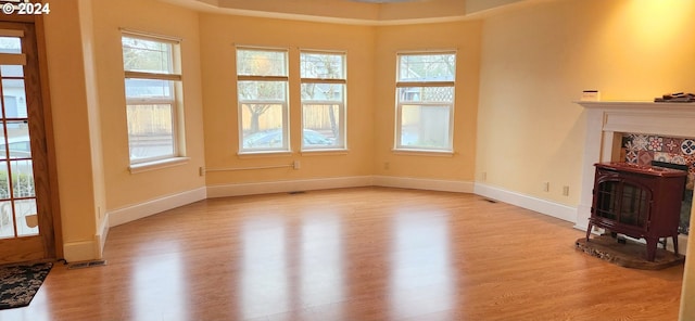 unfurnished living room featuring a wood stove, plenty of natural light, and light hardwood / wood-style floors