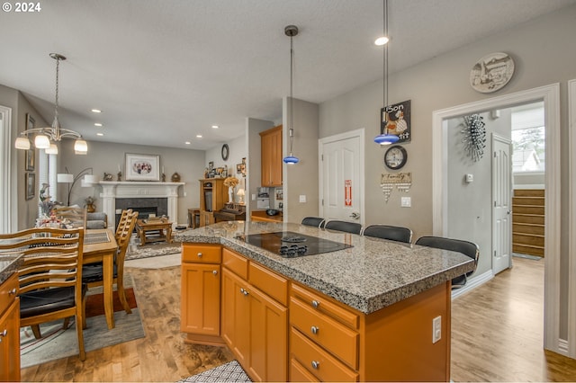 kitchen featuring light wood-type flooring, black electric stovetop, a kitchen island, and hanging light fixtures