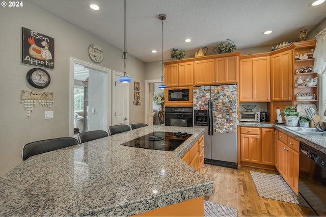 kitchen featuring pendant lighting, light hardwood / wood-style floors, sink, a breakfast bar area, and black appliances