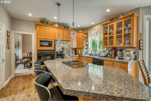 kitchen with a breakfast bar, pendant lighting, a center island, light hardwood / wood-style flooring, and black appliances