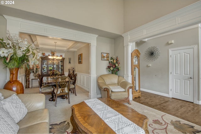 carpeted living room with ornamental molding, an inviting chandelier, a raised ceiling, and ornate columns