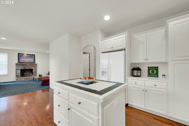 kitchen featuring white fridge with ice dispenser, tile countertops, a center island, white cabinets, and light hardwood / wood-style floors