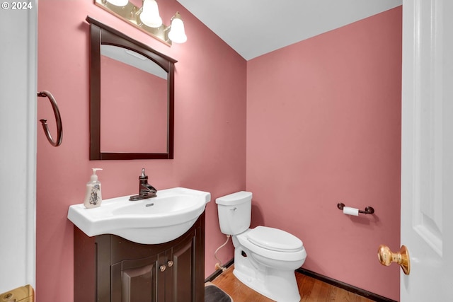 bathroom featuring toilet, hardwood / wood-style flooring, vanity, and vaulted ceiling