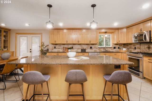 kitchen with a kitchen bar, appliances with stainless steel finishes, a center island, and decorative light fixtures