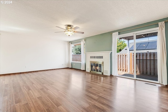 unfurnished living room featuring a textured ceiling, hardwood / wood-style floors, and a brick fireplace