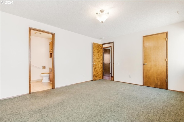 unfurnished bedroom featuring ensuite bath, a textured ceiling, and light colored carpet