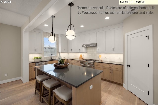 kitchen with hanging light fixtures, sink, stainless steel stove, a kitchen island, and white cabinetry