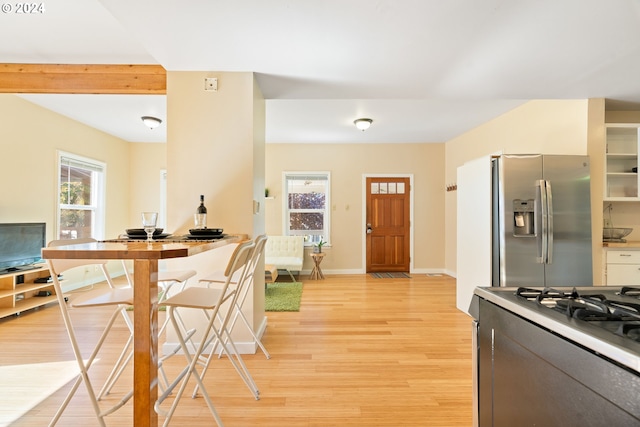 kitchen with light wood-type flooring, baseboards, stainless steel refrigerator with ice dispenser, and range with gas cooktop