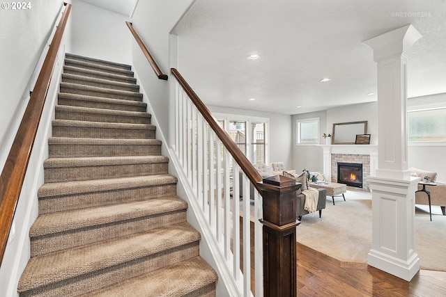 stairs with ornate columns, hardwood / wood-style floors, and a stone fireplace