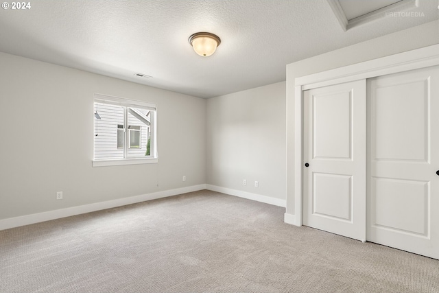 unfurnished bedroom with a closet, light colored carpet, and a textured ceiling