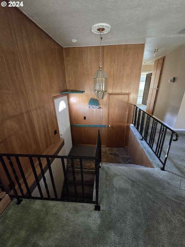 staircase with carpet floors, a textured ceiling, and wooden walls