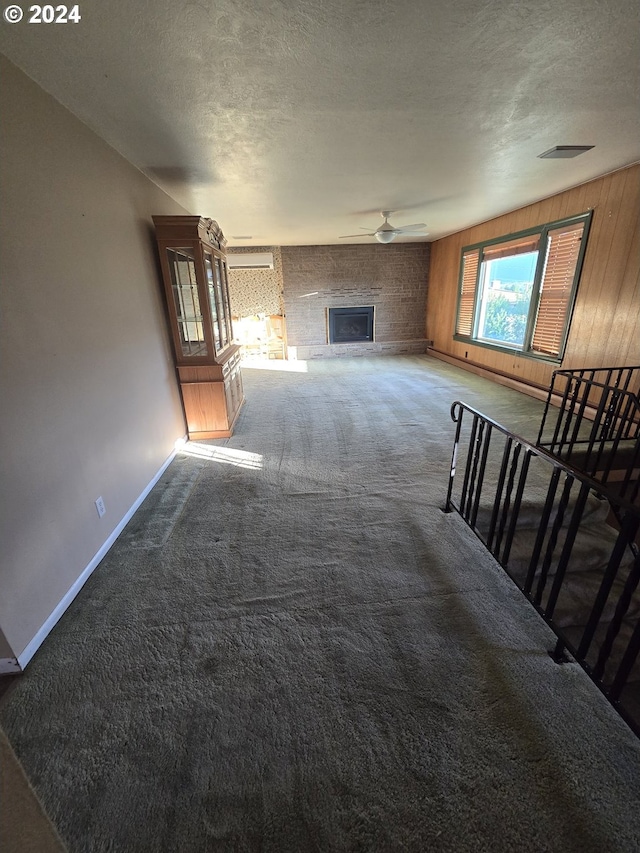 unfurnished living room featuring ceiling fan, a large fireplace, carpet, wood walls, and a textured ceiling