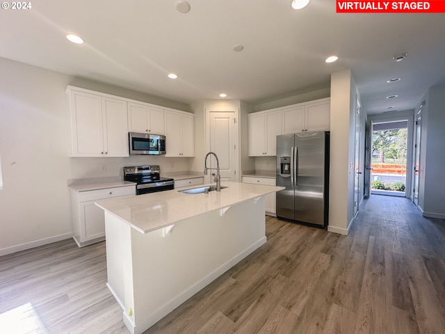 kitchen with appliances with stainless steel finishes, a kitchen island with sink, sink, and white cabinets