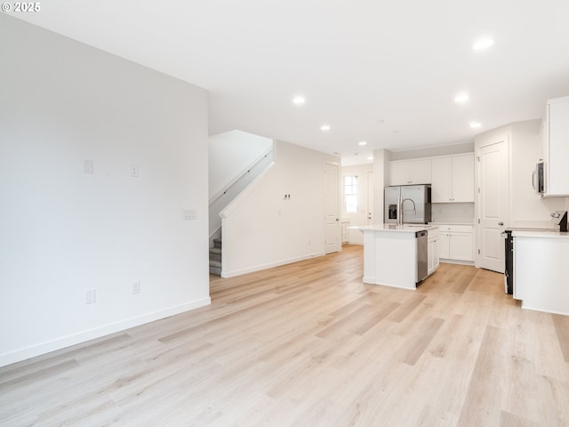 kitchen with stainless steel appliances, light hardwood / wood-style floors, a center island with sink, and white cabinets