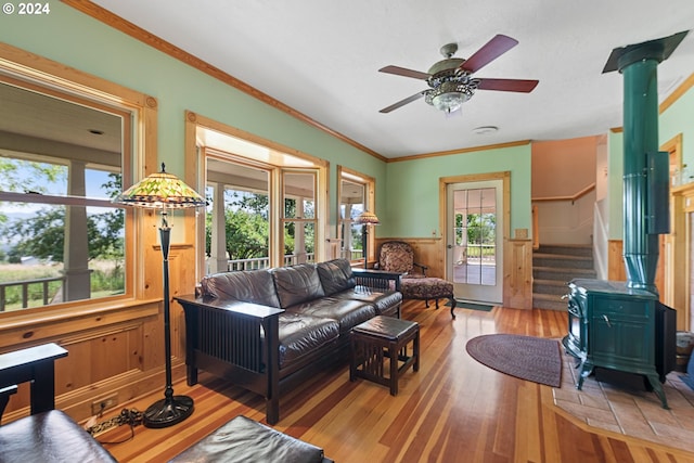 living room featuring crown molding, light hardwood / wood-style floors, ceiling fan, and a wood stove