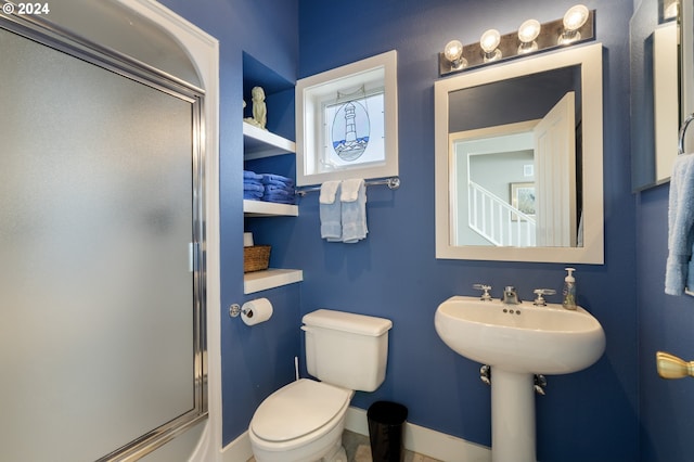 bathroom featuring a shower with door, sink, and toilet