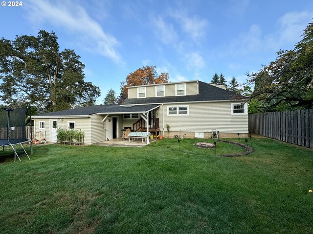 rear view of property featuring a lawn, a trampoline, and a patio area