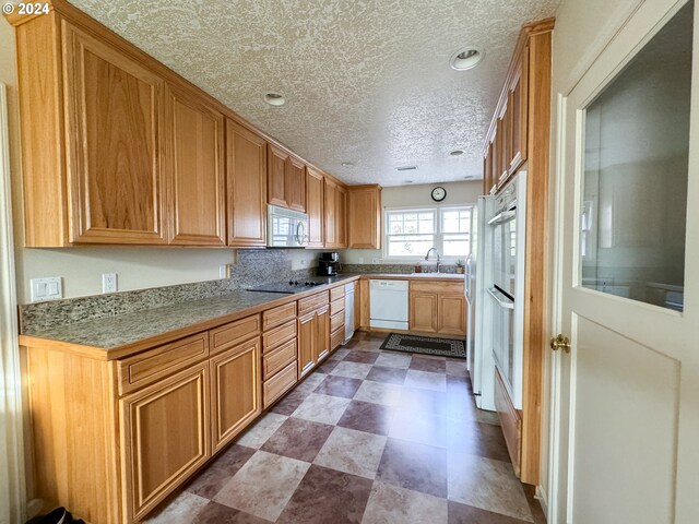 kitchen featuring black electric cooktop, dishwasher, sink, and a textured ceiling