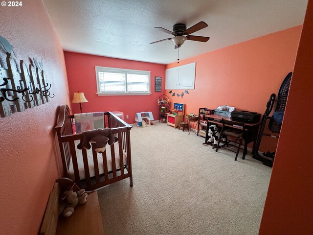 carpeted bedroom with ceiling fan, a nursery area, and a textured ceiling