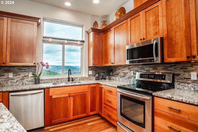 kitchen featuring sink, light hardwood / wood-style flooring, tasteful backsplash, light stone counters, and stainless steel appliances