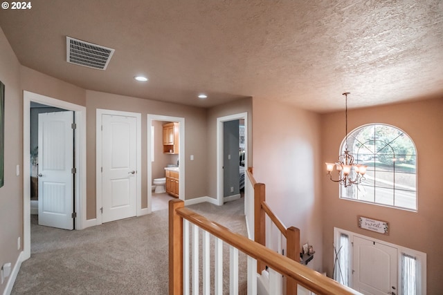 hall with light colored carpet, a notable chandelier, and a textured ceiling