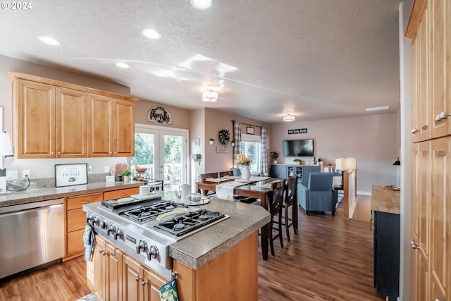 kitchen featuring stainless steel appliances, wood-type flooring, a textured ceiling, and a kitchen island