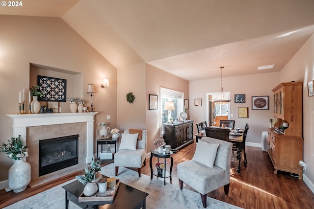 living room with wood finished floors, a tile fireplace, baseboards, and vaulted ceiling