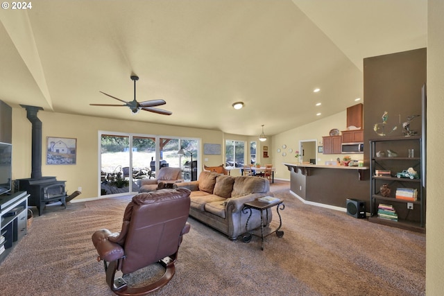 carpeted living room with vaulted ceiling, a wood stove, and ceiling fan