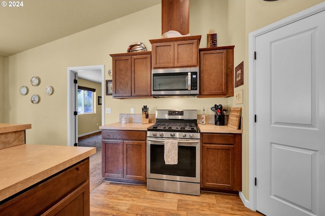 kitchen featuring appliances with stainless steel finishes, light wood-type flooring, and lofted ceiling