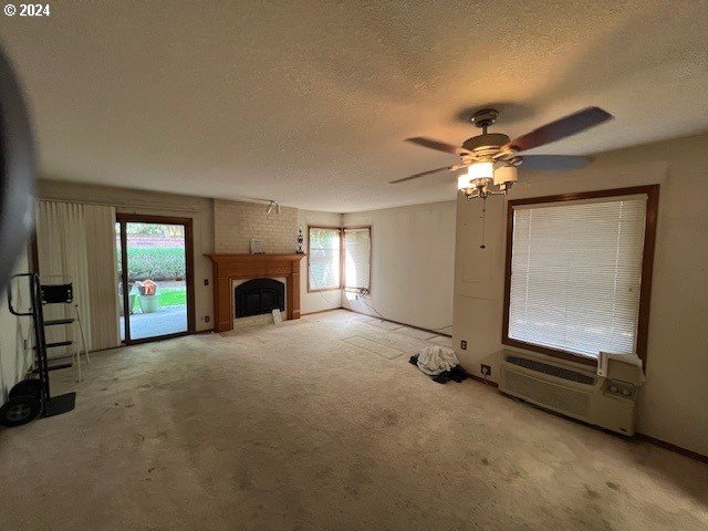 unfurnished living room with light colored carpet, ceiling fan, a textured ceiling, and a fireplace