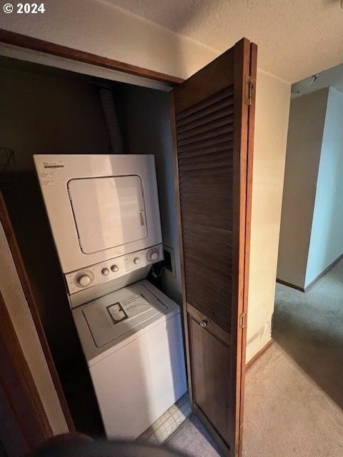 clothes washing area with light carpet, a textured ceiling, and stacked washer and clothes dryer