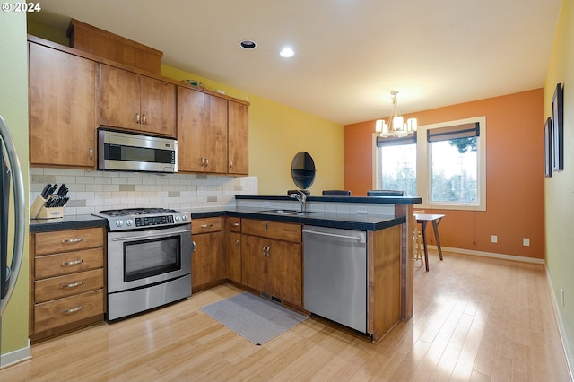 kitchen with pendant lighting, appliances with stainless steel finishes, light hardwood / wood-style floors, kitchen peninsula, and a chandelier